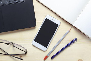 Office desk top view with smartphone, laptop, eyeglasses and books