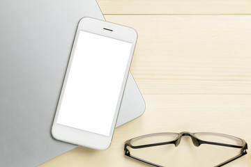 Mobile smartphone white screen with laptop and eyeglasses on wood desk top view