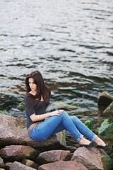 Young beautiful brunette girl with long hair sitting on the rocks by the sea  a background of dark green waves.