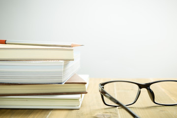 Eyeglasses, books and pencil on wood table, selective focus