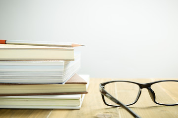 Eyeglasses, books and pencil on wood table, selective focus