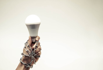 Hand holding a turned on LED light bulb chained and lock / Something stops new idea / Freedom of thought © weerapat1003