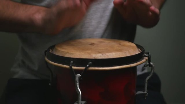 Playing a small bongo with two hands.