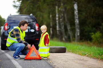 Father and his little son repairing car and changing wheel together