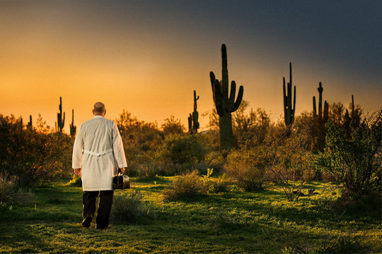 Doctor In A Lab Heading Off Into A Desert Sunset With A Medical Bag In His Hand.  The Landscape Is Filled With Saguaro Cactus.