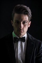 Obraz premium Young businessman confidently posing and looking at camera, wearing suit, on dark background