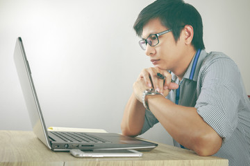 Young asian man working seriously on laptop with smartphone on desk