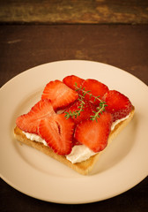 Toasted bread with cream cheese, strawberries and thyme on wooden table