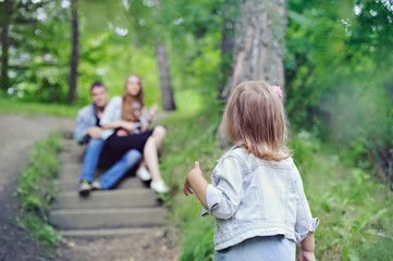 Fototapeta premium Family on the walk, a little girl stands back and looks at his parents in the background.