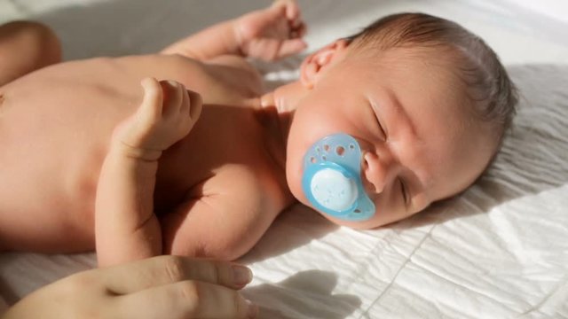 Closeup shot of mother giving soother to hew newborn baby son lying on bed in sun rays