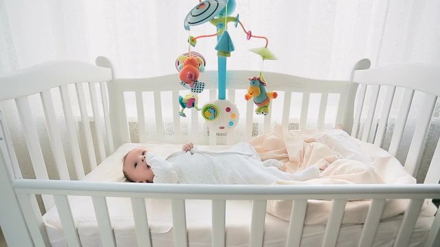 Cute 3 months old baby playing with mobile in white wooden crib