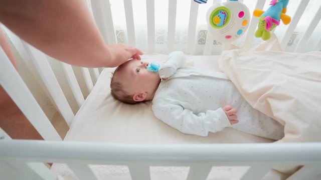 Young caring parent caressing cute 3 months old baby boy lying in cot