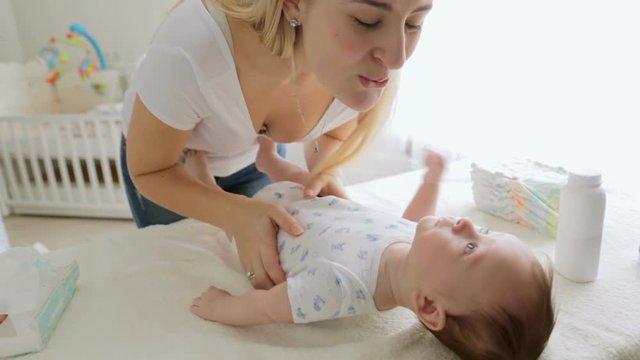 Closeup of young cheerful mother talking to her baby boy and playing with him