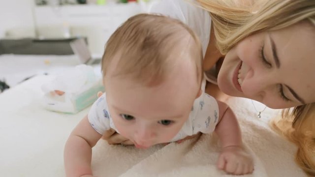 Closeup shot of cute 3 months old baby boy crawling on bed with his beautiful young mother