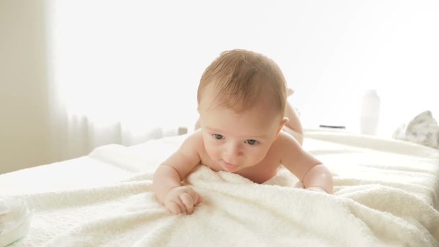 Cute 3 months old baby boy lying on bed and trying to crawl.