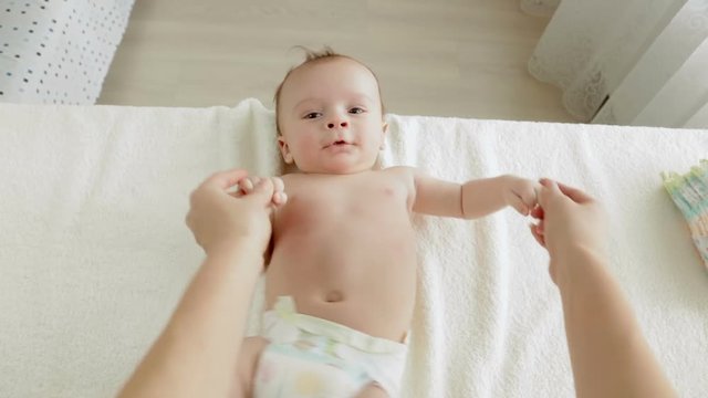 POV of young mother holding hands and looking at cute baby boy lying on changing table
