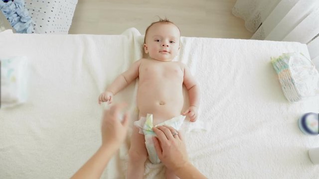 POV young mother taking dirty diapers of adorable baby boy lying on table