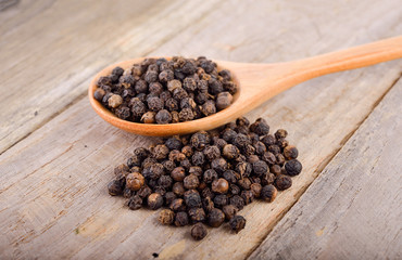 dried black pepper grain on wooden spoon and on the table