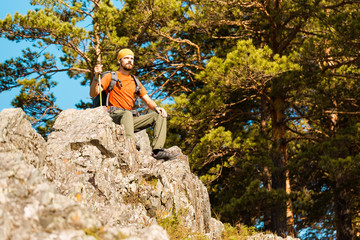 Naklejka na ściany i meble Young male with beard is traveling through the mountain, tourist rucksack standing on rock hill while enjoying nature view, summer holidays in mountains