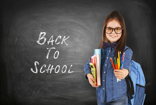 School concept. Cute girl with backpack holding book on blackboard background. Text back to school.