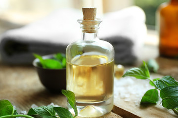 Bottle with mint oil and fresh leaves on wooden table
