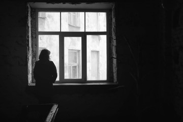 Concept of loneliness in the city, waiting and decision making. Woman looking out of the window in...
