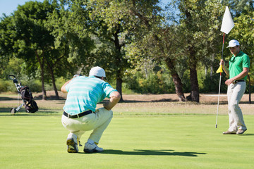 Golf. One golfer reading green, other holding flag