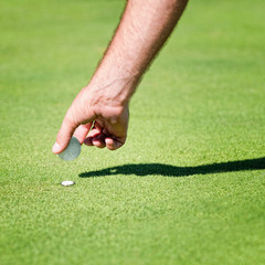 Golfer placing golf ball on the green