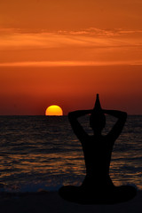Silhouette of young woman practicing yoga on the beach at sunris