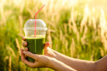 green energy and nutritional smoothie drink cocktail with banana, mint, lettuce, fennel, lime, cucumber, useful in the hands of a young girl on the background blurred nature