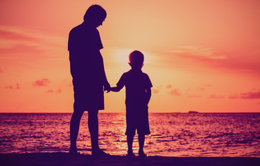 silhouette of father and son holding hands at sunset sea