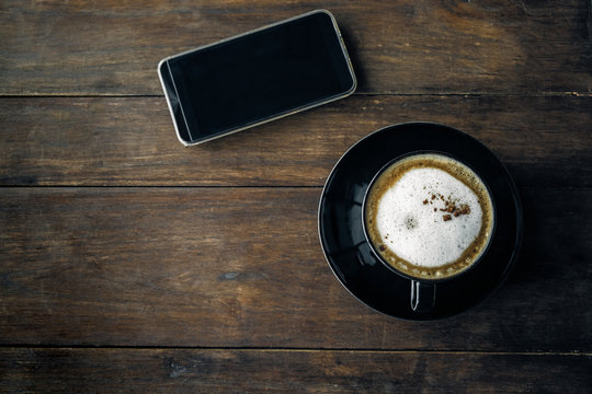 Coffee cup on wooden table background with smartphone,Top view, Selective focus.
