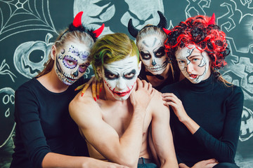 Fototapeta premium Three girls and a guy with Halloween face art on dark background pattern
