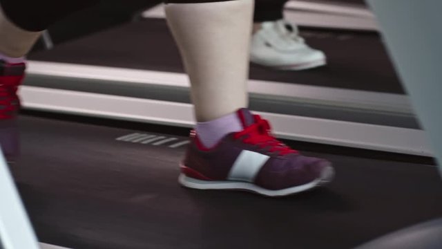 Closeup of fatty female legs in sport shoes walking on moving treadmill desk in the gym