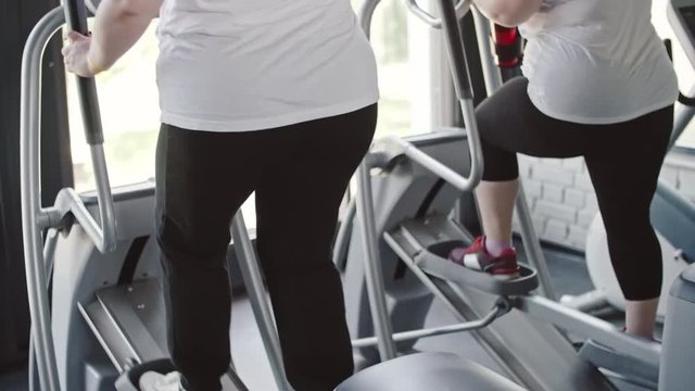 Tilt up of two overweight women working out on elliptical machines in the gym