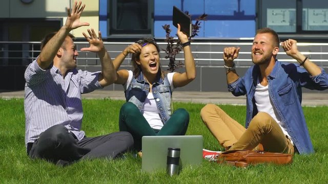 happy students sitting on the lawn and sing