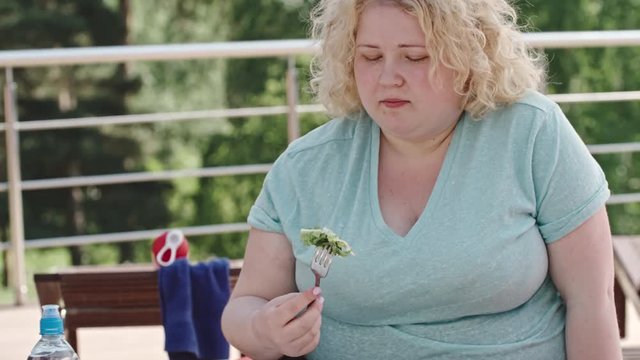 Tilt up of overweight blonde woman forcing herself to eat green salad on a diet