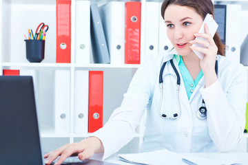 Closeup portrait of a attractive female doctor talking on the mobile phone with patient looking at the laptop screen.