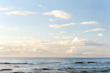 White fleecy clouds above the sea on blue sky background.