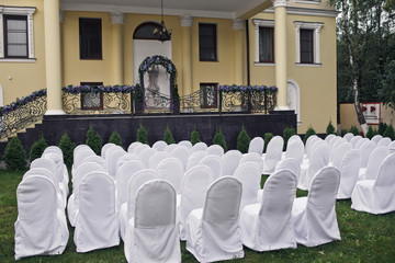 Chairs covered with white cloth stand before the porch with wedd