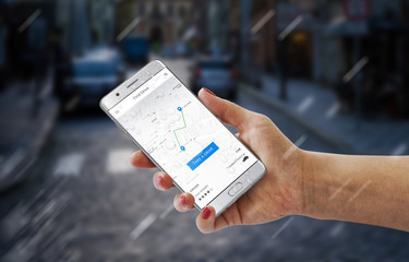 Driver hire app on modern smartphone in woman hand. City street in background.