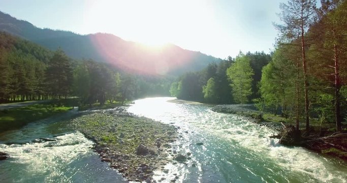 4k (UHD) aerial view. Low flight over fresh cold mountain river at sunny summer morning. Green trees and sun rays.