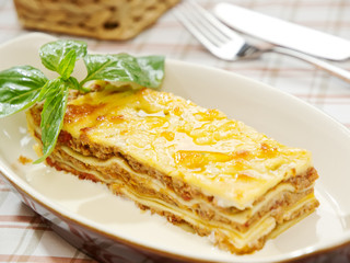 traditional lasagna made with minced beef bolognese sauce topped with basil leafs served on a white plate