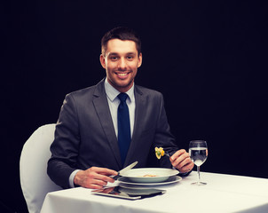 smiling man with tablet pc eating main course