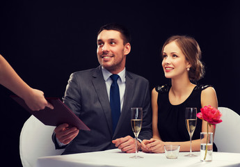 waiter giving menu to happy couple at restaurant