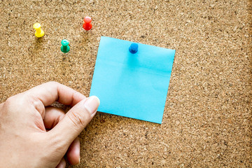 Hand holding reminder sticky note on cork board