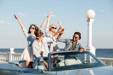 Joyful young people giving high five and driving cabriolet