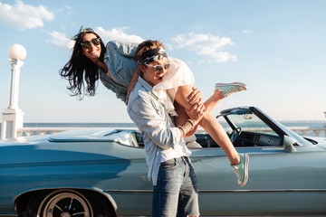 Man carrying his woman and having fun near vintage cabriolet