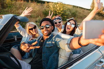 Happy young people taking selfie with smartphone in the car