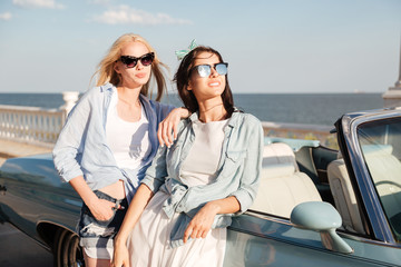 Two happy young women standing and waiting near cabriolet